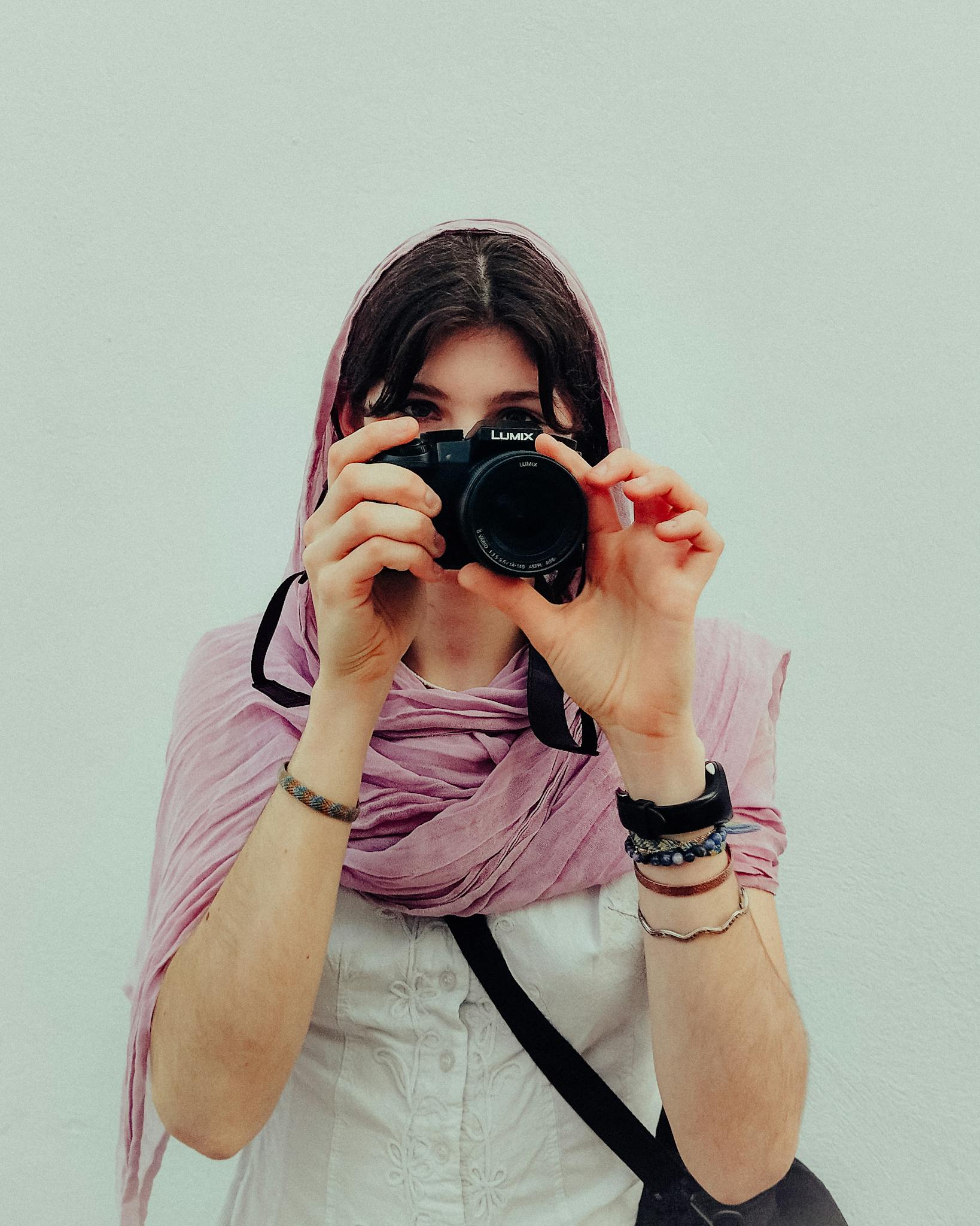A woman in a pink scarf takes a picture, capturing a classic photographer's moment.