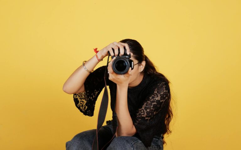 A young female photographer taking a photo with a DSLR camera against a yellow background.