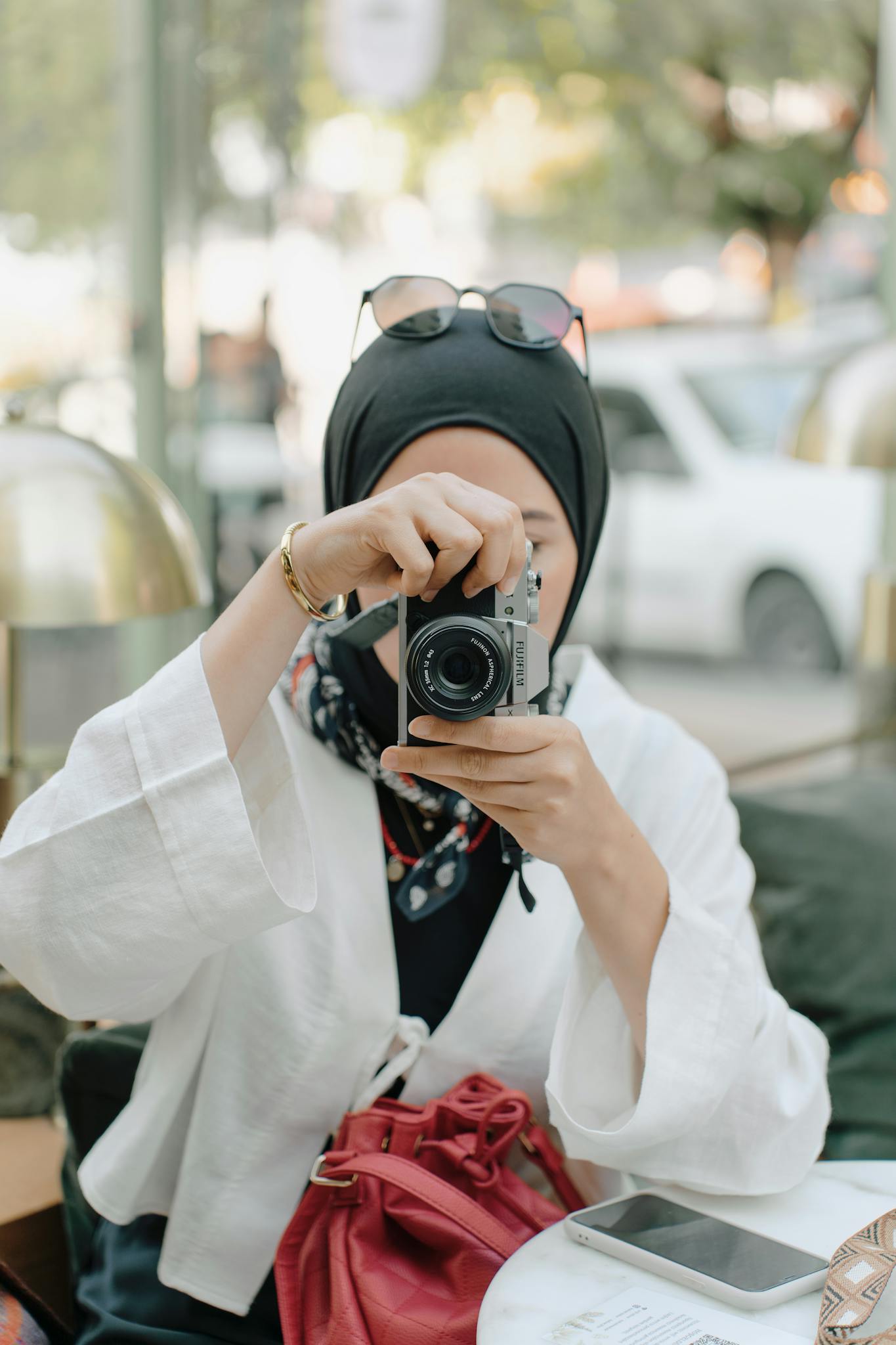 Stylish woman captures urban life at a café in Ankara, Türkiye, using a camera.