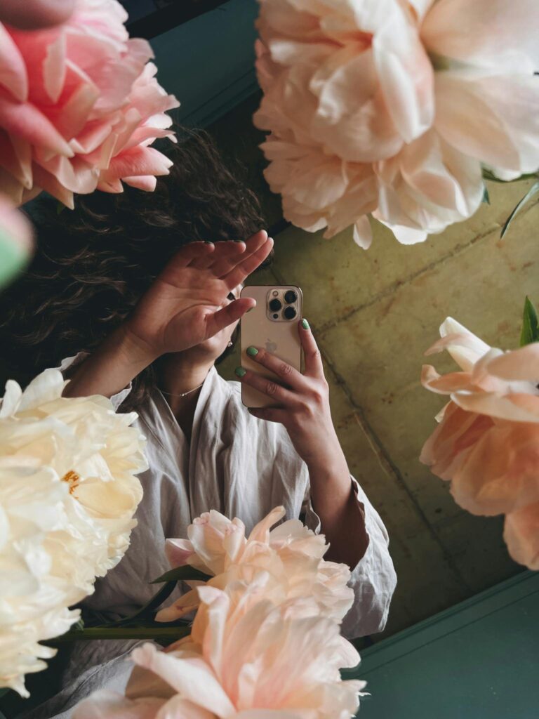 Woman taking a selfie through flowers, blending technology and nature.